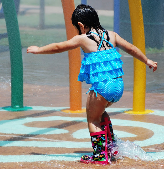 Little girl wears galoshes at a spray ground