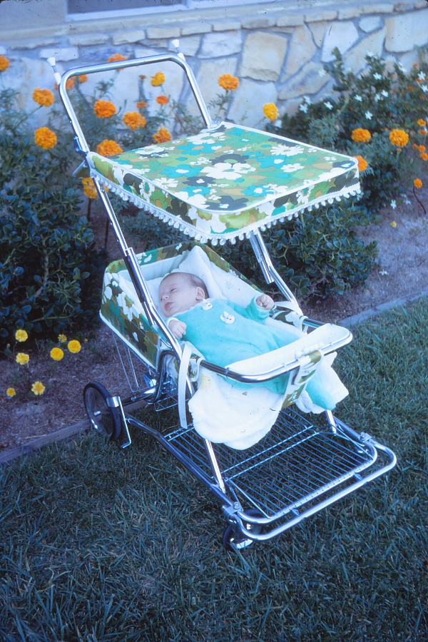 1970s Baby Equipment | A 1970 Baby Stroller in avocado green and turquoise floral with white pom pom fringe on the sunshade. 